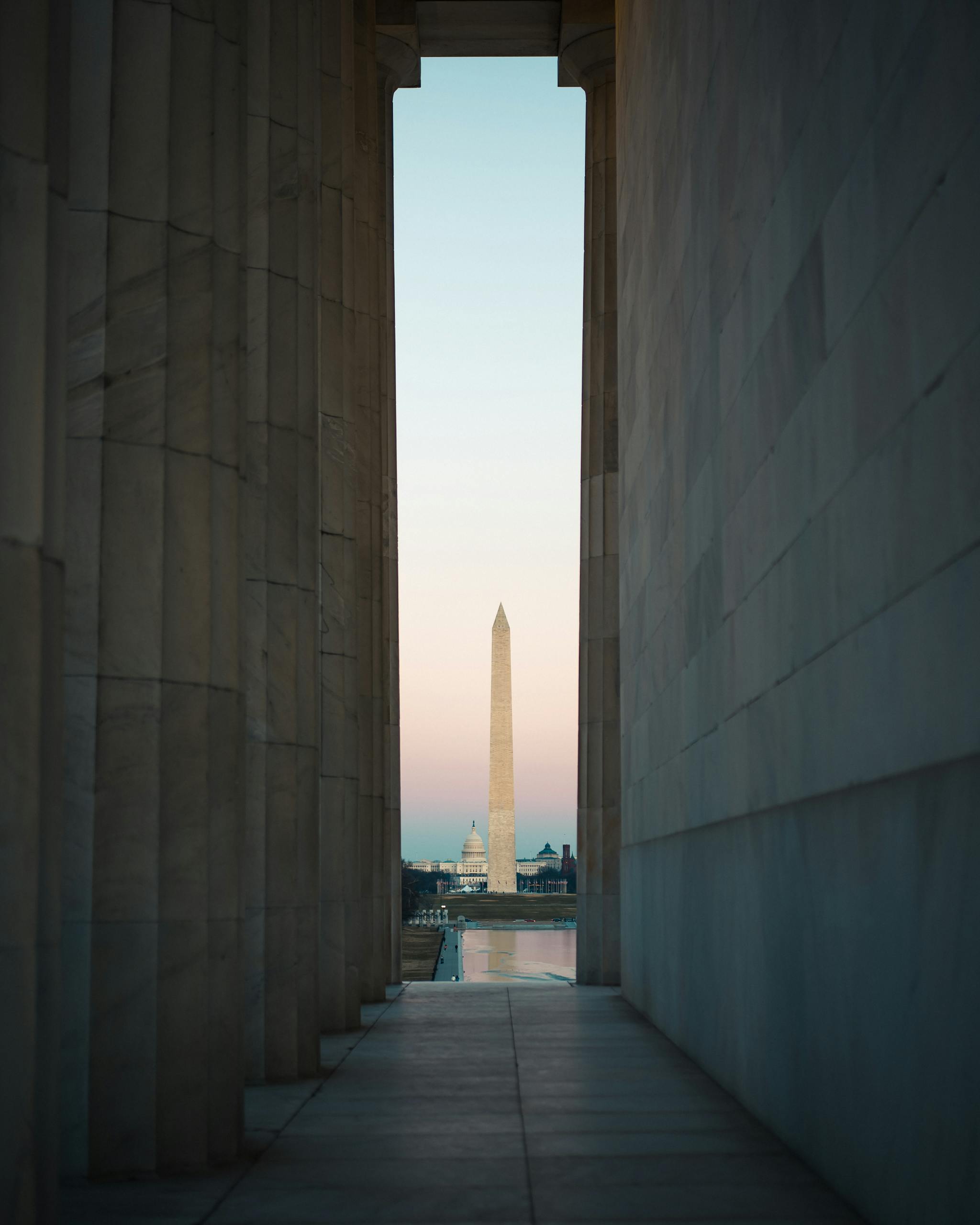 View of the Washington Monument through Lincoln Memorial columns at sunset in Washington, DC.